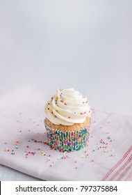 Vanilla Cupcake Decorated With Sprinkles On The Kitchen Towel, White Background, Space For Text Above.