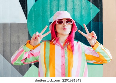 Vanilla Girl. Kawaii vibes. Candy colors design. Young woman with pink hair and sunglasses in Bucket hat and multicolor strippled shirt making V sign by fingers. Anime Urban street fashion. - Shutterstock ID 2291681343
