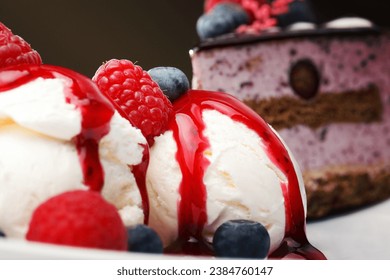 Vanilla ice cream with fresh raspberries and blueberries topped with a red fruity berry coulis , close up view