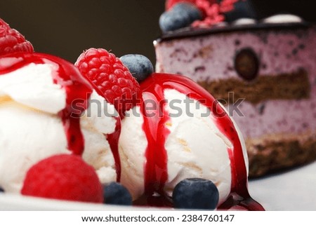 Vanilla ice cream with fresh raspberries and blueberries topped with a red fruity berry coulis , close up view