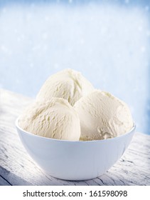 Vanilla ice-cream scoops in white cup over snow background.