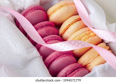 vanilla and raspberry macaroons in a box on a white napkin, sweet gift with a pink ribbon