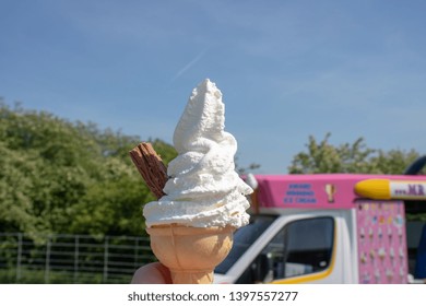 Vanilla white cold Ice cream and ice cream cone with a chocolate flake sticking out the side taken outside ab ice cream van on a sunny day showing the clear blue sky and blurred trees in age back. - Powered by Shutterstock