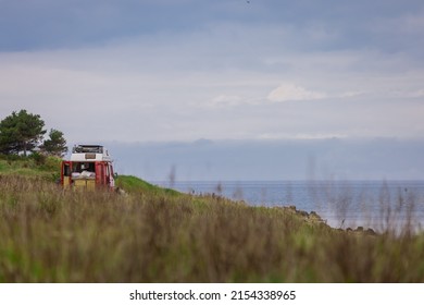 Vanlife Or Van Life In Its Fullest. Red Vintage Old Van With Visible Bed In The Back Parked In The Middle Of Nature Overlooking The Sea On A Cloudy Day. Freedom With A Van.