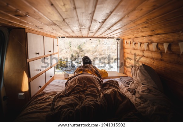 Vanlife - Young woman lying in camping van and\
looking at beautiful\
nature