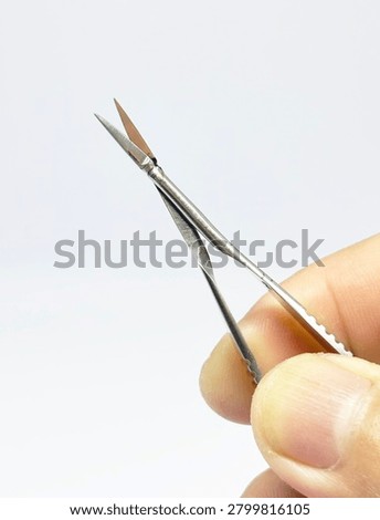 Vannas microsurgical scissors held between fingers against a white background