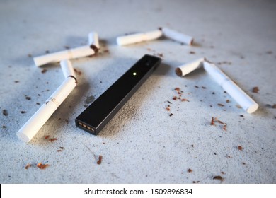 Vape Device Electronic Cigarette Juul, As Smoking Alternative With Broken Marlboro Gold Cigarettes And Scattered Tobacco On White Textured Background