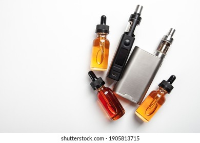 Vape juice next to smoking devices. Bottles with vape juice on a white table. Devices for vaping and vape juice nearby. Top view vaper set. E-cigarette refills. Liquids for vaping devices