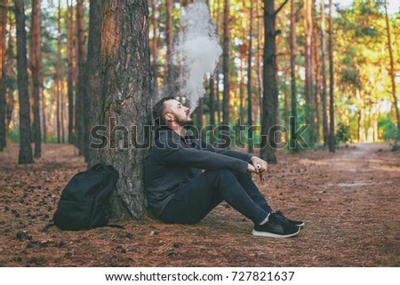 Vape man. brutal bearded young man having rest in forest and vaping an electronic cigarette. Lifestyle. Vape concept