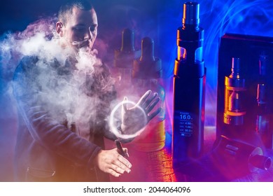 Vape Pen And Juice Next To Smoker. Guy Does Vape Smoke Tricks. Vaper In Dark In Neon Color. Concept - Buying A Vape Pen. Young Man Made A Ring From Cigarette Vapor. He Smokes Electronic Cigarette.