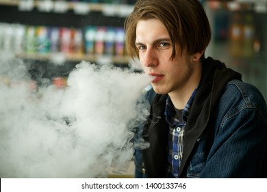 Vape Teenager. Portrait Of Young Handsome Guy Smoking An Electronic Cigarette In The Vape Bar. Bad Habit That Is Harmful To Health. Vaping Activity. Close Up.