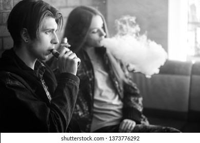 Vape Teenagers. Young Cute Girl In Sunglasses And Young Handsome Guy Smoke An Electronic Cigarettes In The Vape Bar. Bad Habit That Is Harmful To Health. Vaping Activity. Black And White.