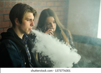 Vape Teenagers. Young Cute Girl In Sunglasses And Young Handsome Guy Smoke An Electronic Cigarettes In The Vape Bar. Bad Habit That Is Harmful To Health. Vaping Activity.