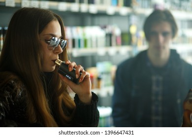 Vape Teenagers. Young Cute Girl In Sunglasses And Young Handsome Guy Smoke An Electronic Cigarettes In The Vape Bar. Bad Habit That Is Harmful To Health. Vaping Activity.