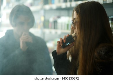 Vape Teenagers. Young Cute Girl In Sunglasses And Young Handsome Guy Smoke An Electronic Cigarettes In The Vape Bar. Bad Habit That Is Harmful To Health. Vaping Activity.