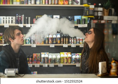 Vape Teenagers. Young Cute Girl In Sunglasses And Young Handsome Guy Smoke An Electronic Cigarettes In The Vape Bar. Bad Habit That Is Harmful To Health. Vaping Activity.