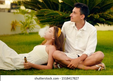 A vape woman and man. Couple on vacation, under a palm tree. Rest, smoking, nicotine, pleasure, danger. Vape liquid. Vaping THC e cigarette.