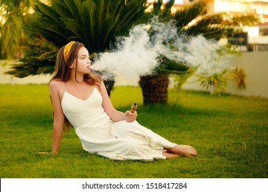A vape woman on vacation, under a palm tree. Rest, smoking, nicotine, pleasure, danger. Vape liquid. Vaping THC e cigarette.