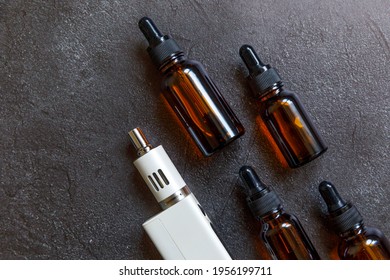 Vaping device e-cigarette electronic cigarette and liquid bottles on dark black stone shale background. Vape device for alternative smoking. Vaping shop concept. Gadget for vaper. Vaping accessories