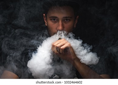 vaping man holding a mod. A cloud of vapor. Black background.