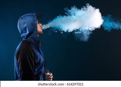 vaping man holding a mod. A cloud of vapor. dark blue background.