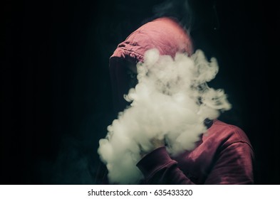 Vaping man holding a mod. A cloud of vapor. Black background. Vaping an electronic cigarette with a lot of smoke. Vape concept