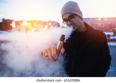 vaping man holding a mod device. cloud of vapor. Vape. high contrast and monochrome color tone. e-cig device