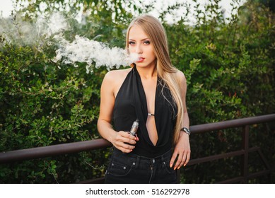 Vaping. Young beautiful woman smoking ( vaping ) e-cigarette with smoke outdoors. Vapor concept.