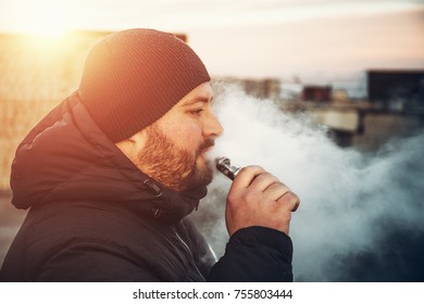 Vaping Young Man Holds Electronic Cigarette Or Vape Pen In Hand And Smokes, Toned