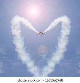 Vapour Trail From Stunt Planes Making A Love Heart In The Blue Sky. Artistic Solar Flare Added For Drama