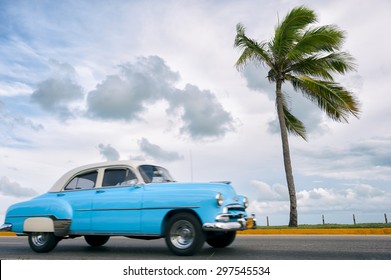 VARADERO, CUBA - CIRCA JUNE, 2011: Classic vintage American car drives along a coastal road next to single palm tree.
