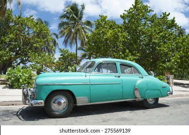 VARADERO, CUBA - JUNE, 2011: Classic American car stands parked in front of palm trees on the road next to the beach.