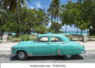 VARADERO, CUBA - JUNE, 2011: Classic vintage American car stands parked in front of palm trees on the road next to the beach.