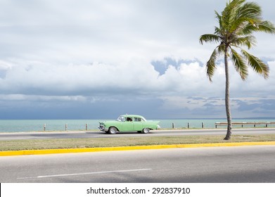 VARADERO, CUBA - JUNE, 2011: Classic vintage American car drives along an empty coastal road next to single palm tree.