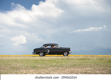 VARADERO, CUBA - JUNE, 2011: Classic vintage American car drives along a flat coastal road against a background of tropical clouds.