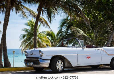 VARADERO, CUBA - JUNE 22, 2015: American white cabriolet Oldtimer parked under palms near the beach