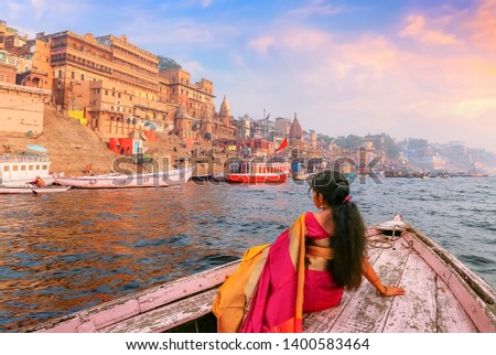 Varanasi ancient city architecture with Ganges river bank at sunset. Indian female tourist enjoy boat ride on the river Ganges