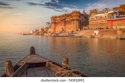 Varanasi Ganges flod ghat med gamle arkitektoniske bygninger og templer som set fra en båd på floden ved solnedgang.