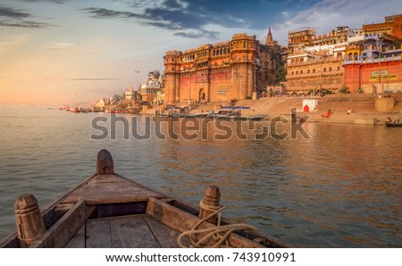 Varanasi Ganges river ghat with ancient architectural buildings and temples as viewed from a boat on the river at sunset.