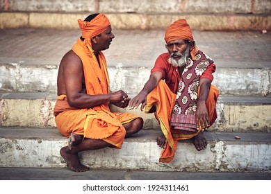 Varanasi, India - 02 17 2020: sadhu pilgrims wearing orange robes talking and meditating by the holy river Ganges