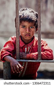 VARANASI, INDIA – MARCH 24: The Ragged Boy Has A Sad Eye, Wearing A Red Shirt Standing On The Fence With A Steel Barrier On March 24, 2018 In Varanasi, India.