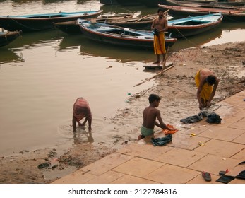 Varanasi, India, November 30,2008: Young Boys And Adult Man Washing Their Clothes With Hands In The Muddy Water Of Sacred Ganges River.