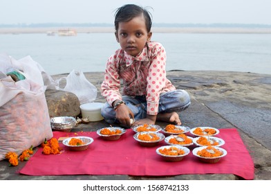 Varanasi, Uttar Pradesh - Nov 12 2019: A Little Poor Boy In Jeans And Shirt Selling Flowers On The Bank Of River Ganges For Pilgrims Who Have Come For Dev Deepavali On Kartik Poornima Or Full Moon Day