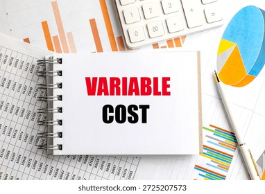 Variable cost phrase on notepad surrounded by financial documents, pen and calculator. 