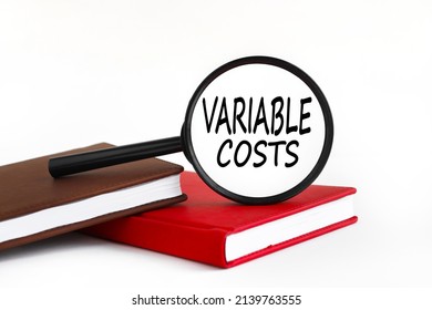 VARIABLE COST text on magnifier glass on white background on red notebook