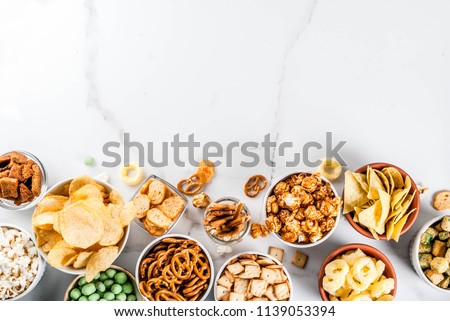 Variation different unhealthy snacks crackers, sweet salted popcorn, tortillas, nuts, straws, bretsels, white marble background copy space