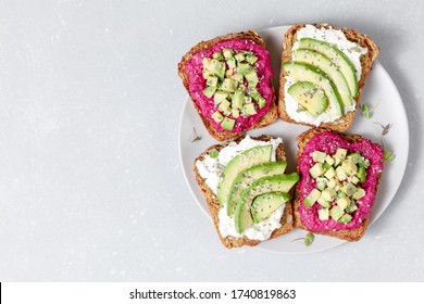 Variation of healthy sandwiches with avocado beetroot cream cheese and whole wheat rye bread on a plate on grey background.   Delicious snacks and toast. Food composition. Top view, copy space