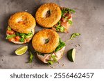 Variety of Bagel sandwiches with ricotta, prosciutto or chicken ham or salmon and microgreens, bagel with ham for breakfast on gray background, close up. Healthy breakfast food.