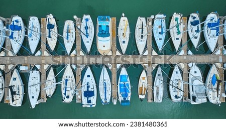 Variety of boats and yachts docked at pier in aerial straight down shot of teal ocean water