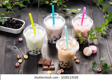 Variety of bubble tea in plastic cups with straws on a wooden table.